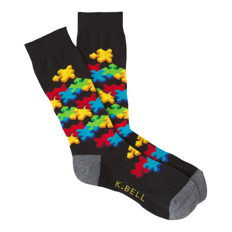 K Bell Mens 3D Puzzle Sock starts on a Black background with Charcoal Grey Heels and Toes.  Under the Cuff starts the Puzzle Pieces of Bright Yellow, Red, Blue and Green. The pieces travel down the Sock to the top of the Foot.