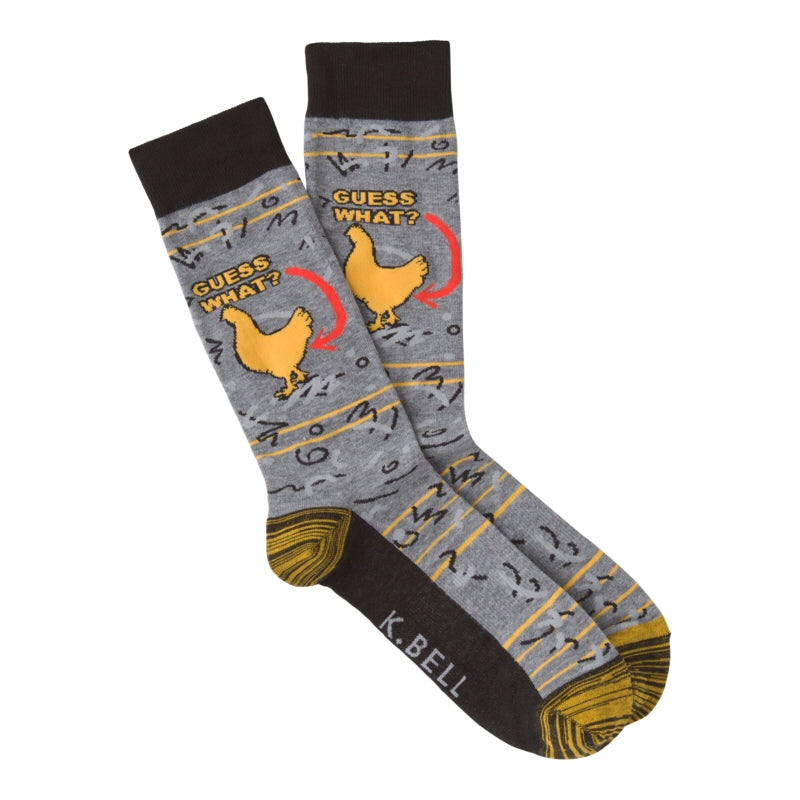 K Bell Mens Chicken Butt Sock starts with a Charcoal Heather background a Black Cuff and Sole, the Heels and Toes are Yellow and Black Stripes. Across the Heather Grey are small Yellow Stripes and Numbers. Then on the Ankle in Yellow you Get in Bold Print "Guess What?" with a Red Arrow. That Red Arrow is Pointing to the back end of a Chicken.