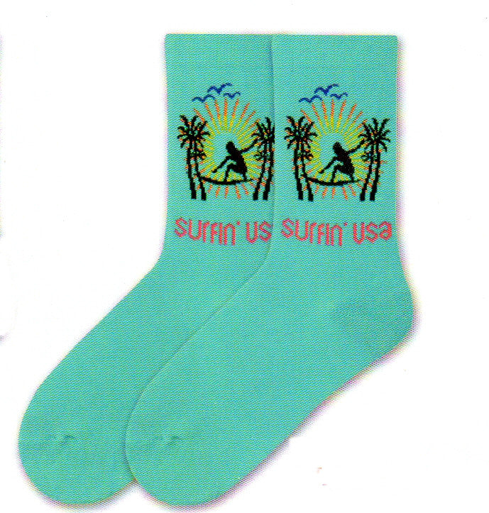K Bell American Made Womens Surfin' USA is on a background called Jewel. A Silhouette of a Girl in Black is on a Surf Board. With Bright Yellow and Orange streams of light. Blue Silhouette of birds. To finish off the scene are Black Palm Tree Silhouettes.