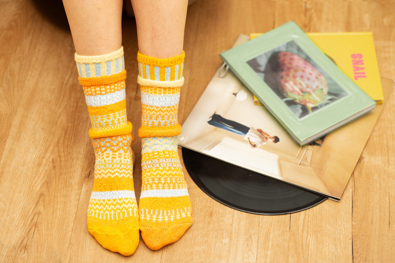 Person wearing yellow patterned socks on a wooden floor with books and a record.