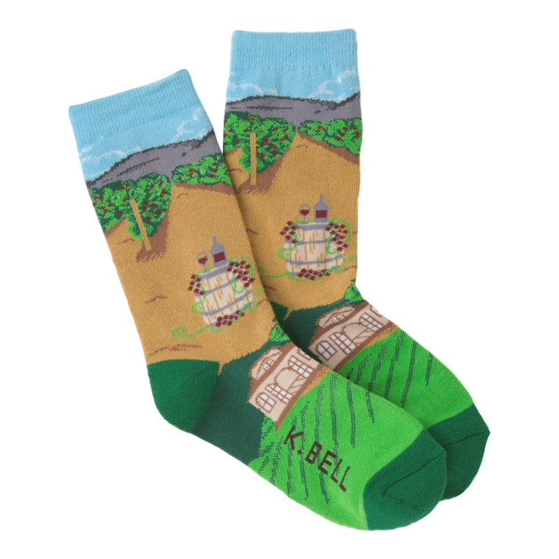 K Bell American Made Womens Winery Sock shows a Barrel with Wine Bottle and Glass in Burgundy for tasting. Then has Rows of Green and Dark Green and Burgundy Grapes growing. The Country House is Tan Chocolate and White with Windows. 