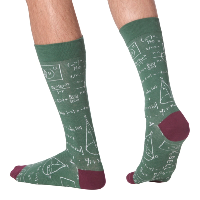 The model is wearing K Bell Mens Equations Sock. This is showing the side and back of the sock. It is Green with Blackberry Heels and Toes. The Equations are all in White  They start below the Cuff and are all over the green.