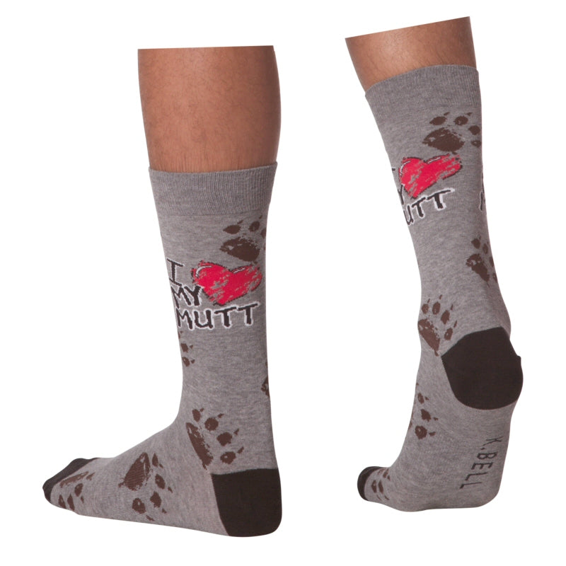 K Bell Mens I Luv My Mutt Sock 2 is on a Model. It starts with a background of Charcoal Heather and Black Heels and Toes. On the Ankle Crew under the Cuff are Big Paw Prints in Taupe.  Then in Bold Print and a Large Red Grey and White Heart and Letters reads, "I Luv My Mutt" Luv = The Heart! Below all this are Taupe Paw prints to the Toes. 