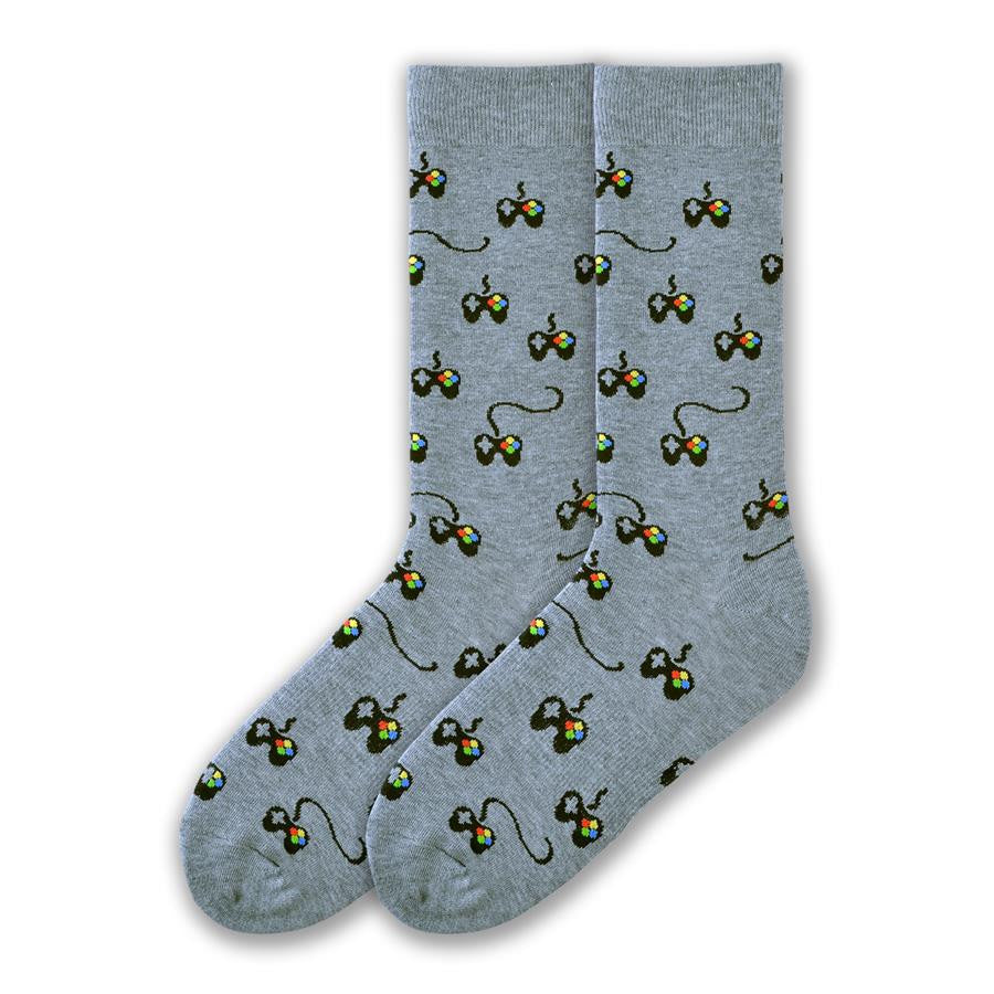K Bell Mens Controller Sock starts on a Grey background with Controllers all over the sock. They are Black with little buttons in Red, Yellow, Blue and Green and a D pad Grey. The cord if it has one is Black.