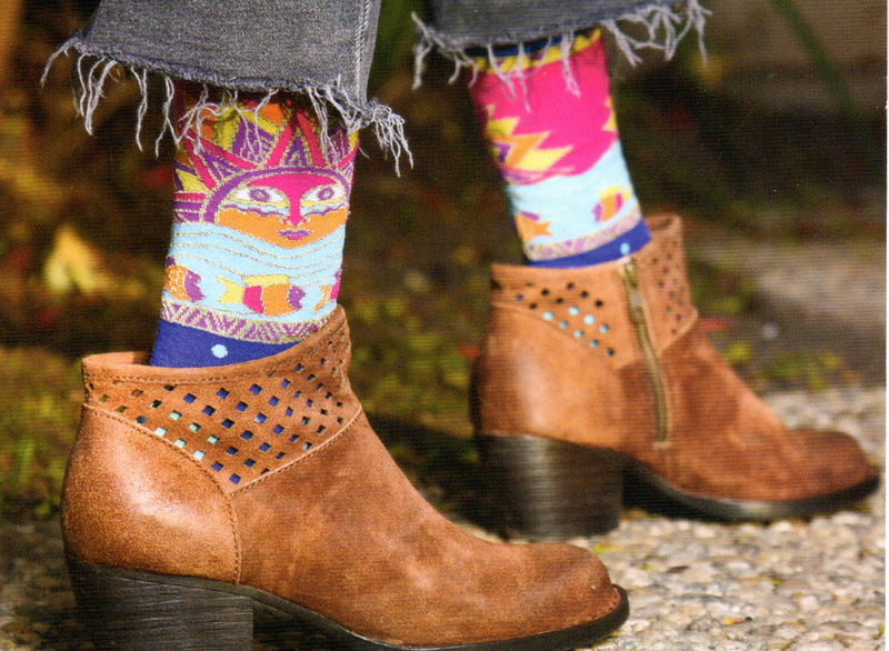 Laurel Burch Sun Fish Sock starts on a Blue Background with Sea Green Cuff Heels and Toes. Bubbles and the River are also Sea Green. The Fish and the Sun are Crimson Plum and Orange with Yellow and Gold Thread. This sock is also featured on a model wearing boots. 