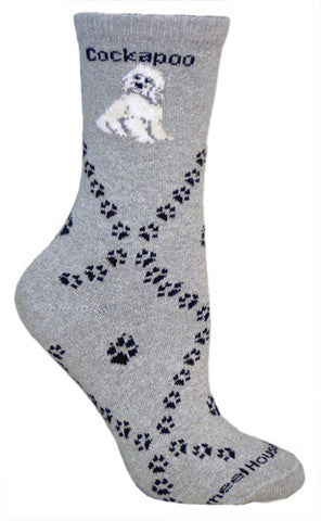 The Cockapoo Sock is on a Grey background with the White Cockapoo at the Top. Cockapoo is in Bold Print below the Cuff. Diamonds are made with Black Dog Paws and in the Center are bigger Dog Paws.