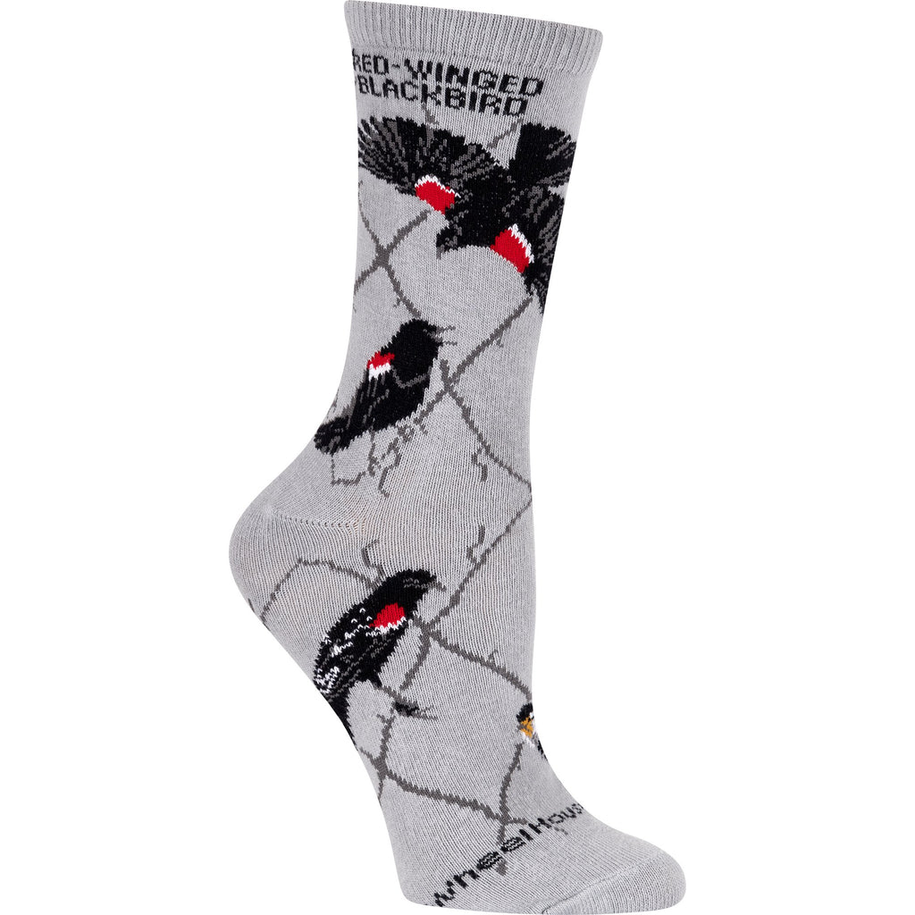 Red-Winged Blackbird Sock by Wheel House Designs starts with a Grey background and a Taupe Argyle Lines. Red-Winged Blackbird is on the Sock below the Cuff. The first Red-Winged is in full flight showing the Red and White on Shoulders. Other Poses include Attacking and Perching. The Female is Posing at the Bottom.